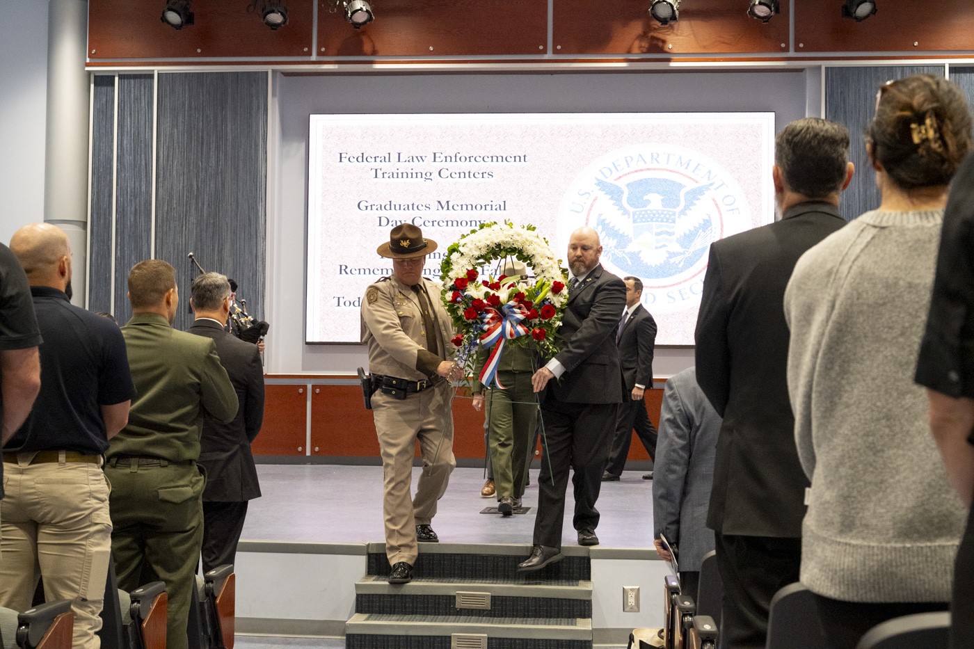 Director Brent W. Nelson and Acting Unit Chief Samuel D. Petruno carry the ceremonial wreath from the stage, joined by FLETC and partner organization representatives in unity to honor the legacy of FLETC graduates who gave their lives in the line of duty, ensuring their memory lives on, Glynco, Ga., May 7, 2025. (FLETC OPA/David Tucker)
