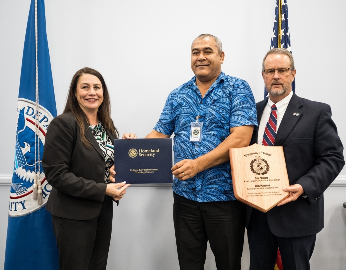 Acting Deputy Director Ariana Roddini presents the graduation certificate to Deputy Commissioner Filipe Fifita, Tonga Police. Deputy Commissioner Fifita was a fellow during DHSLA 22. Division Chief Charles Brewer accepts a plaque from Tonga on behalf of the DHSLA. (FLETC OPA/Mindy Vu)